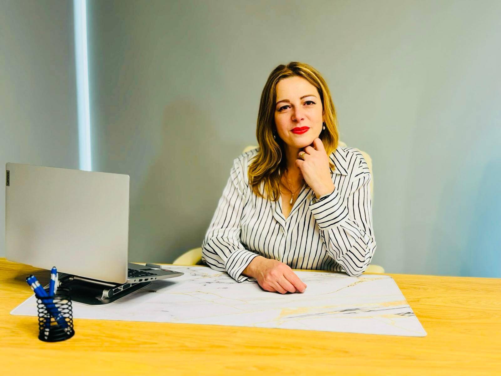 Femeie la birou cu laptop și pixuri albastre.